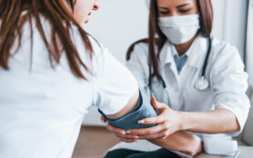 Measuring Blood Pressure. Young Woman Have A Visit With Female Doctor In Modern Clinic