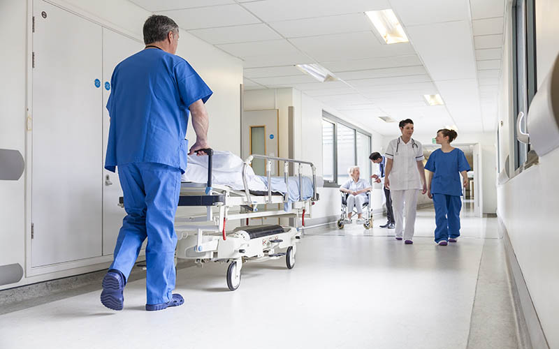 Male,Nurse,Pushing,Stretcher,Gurney,Bed,In,Hospital,Corridor,With