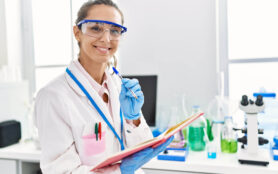 Young,Hispanic,Woman,Wearing,Scientist,Uniform,Writing,On,Notebook,At