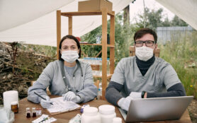Two,Gloved,Clinician,In,Uniform,Working,By,Table,In,Large