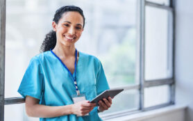 Friendly,Female,Doctor,Smiling,And,Using,Tablet,In,Modern,Hospital